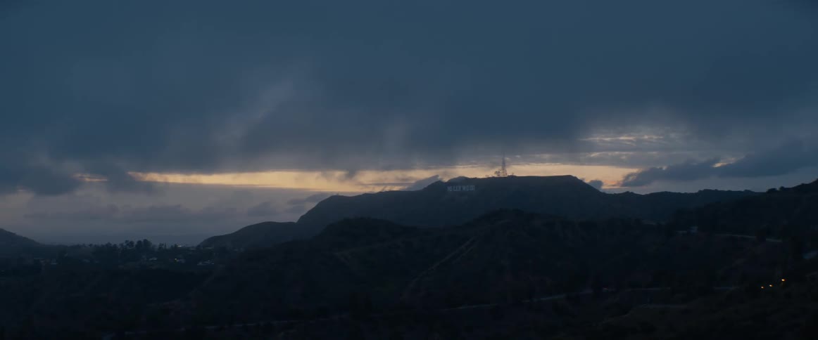 The iconic Hollywood sign is seen in the distance during a moody sunset over the Los Angeles hills