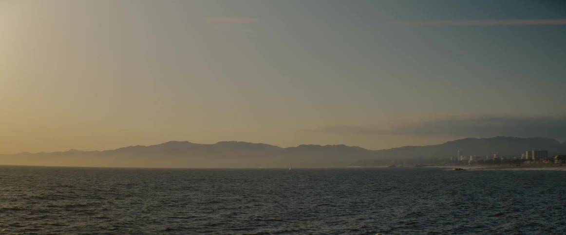 A tranquil ocean view of a hazy mountain coastline during a warm, golden hour sunset