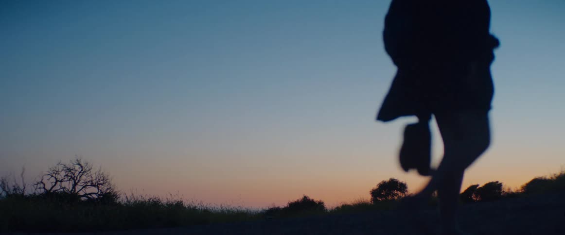 Close-up low-angle shot of a silhouetted person running in slow motion against a peaceful sunset sky
