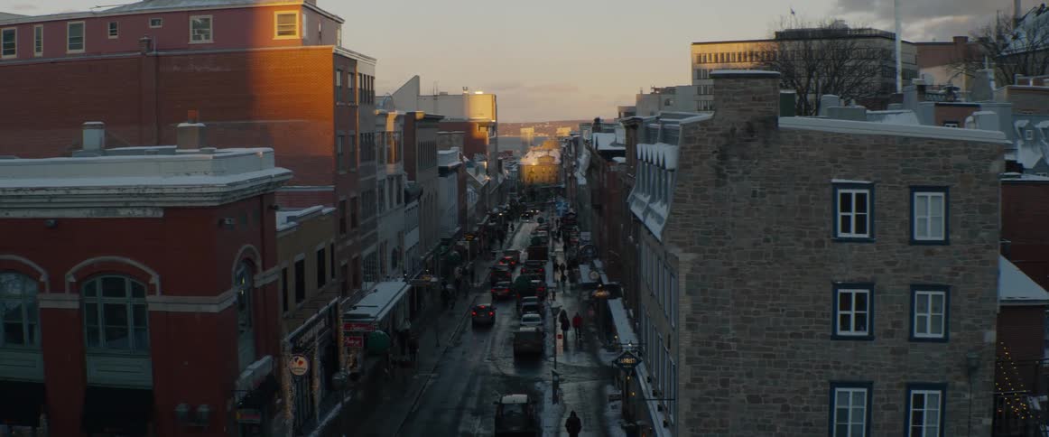 A bustling historic city street is bathed in the warm glow of sunset on a cold winter evening with snow covering the rooftops