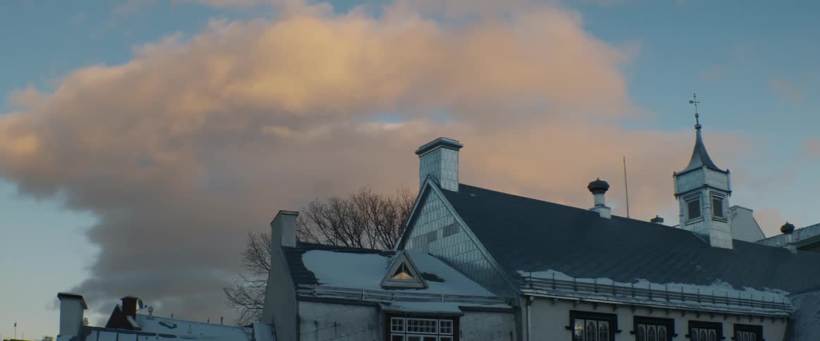 Golden hour clouds drift over the snowy rooftops of a historic building during a cold winter day