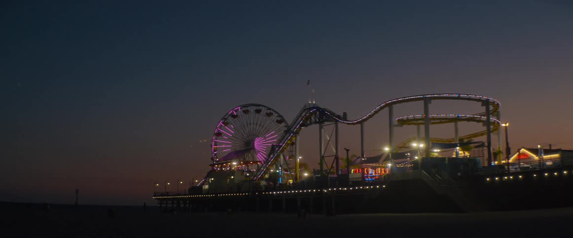 The iconic Santa Monica Pier amusement park glows with colorful lights against the beautiful twilight sky