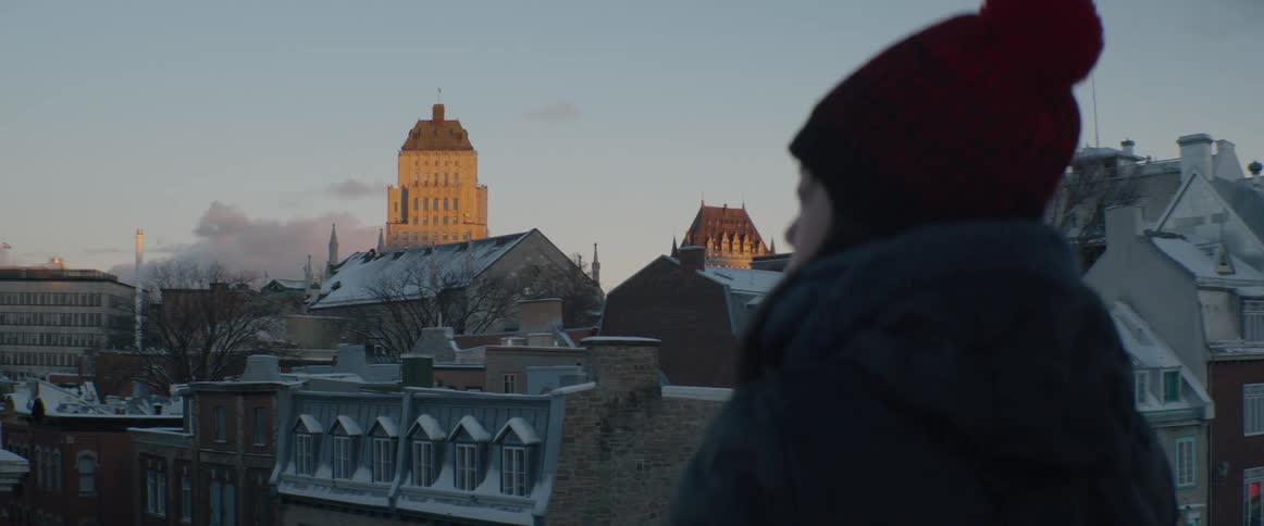 An over-the-shoulder shot shows a person watching the golden hour light hit the historic, snow-covered buildings of Quebec City