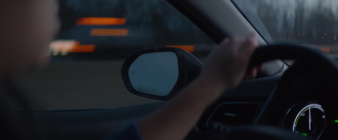 Over-the-shoulder shot of a driver's hand on the steering wheel during a moody twilight drive on the highway