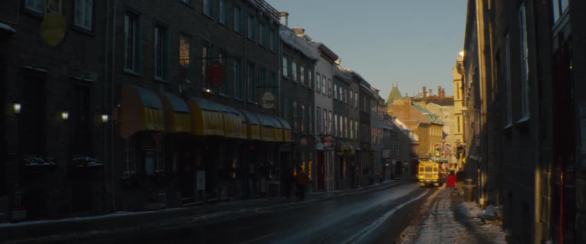 A historic, snow-covered city street is bathed in the warm glow of a winter sunset