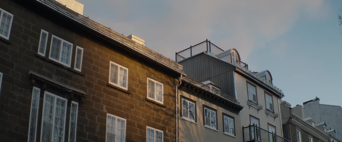 Historic city townhouses with snow-dusted roofs are bathed in the warm golden light of a winter sunset