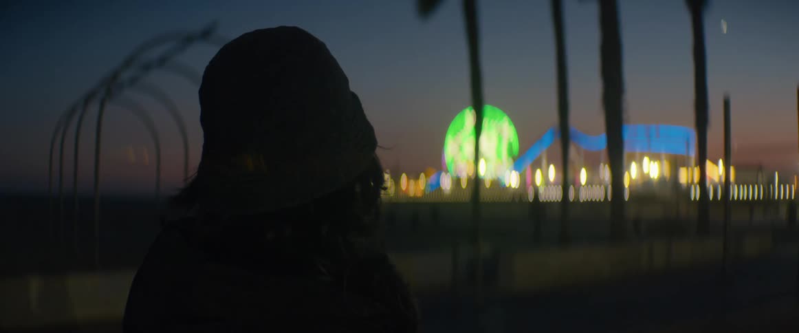 A silhouetted woman watches the colorful bokeh lights of the Santa Monica Pier at dusk