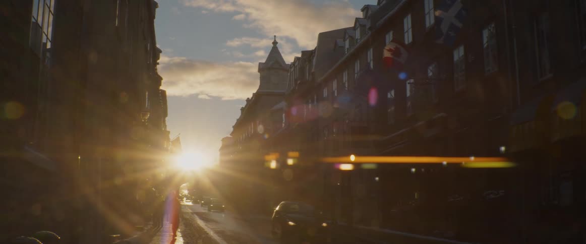 A beautiful sunset casts a golden glow and lens flare over a historic street in Quebec during winter
