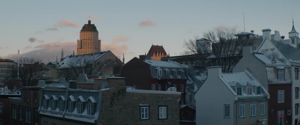 A tranquil winter view of the snow-covered rooftops of Old Quebec City, with the iconic Château Frontenac visible in the distance at dawn
