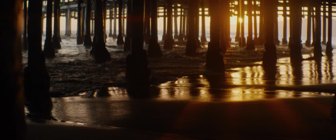 Golden sunset reflects on the wet sand as gentle ocean waves wash ashore under a pier