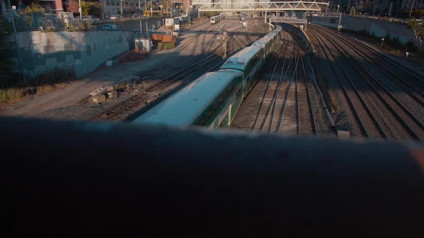 A green and white commuter train travels along urban railway tracks during golden hour as seen from an overpass