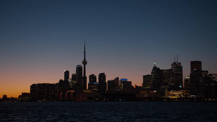 A rack focus shot reveals the Toronto city skyline and CN Tower illuminated against the twilight sky from across the water