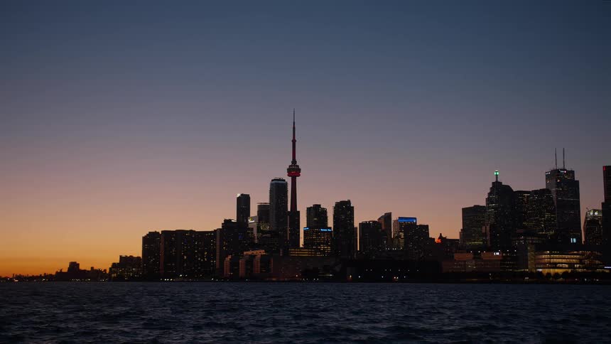 The Toronto city skyline is silhouetted against a beautiful sunset sky as seen from across the water