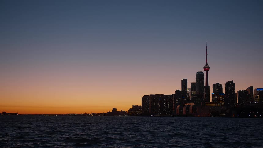 The iconic Toronto skyline is silhouetted against a beautiful orange and purple sunset sky over the water