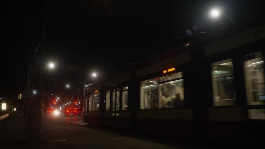 A modern streetcar with bright headlights passes by on a dark city street at night