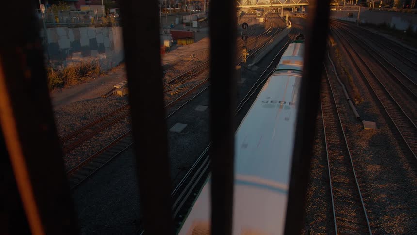 High-angle view through a railing of a passenger train traveling on the tracks during a golden hour sunset