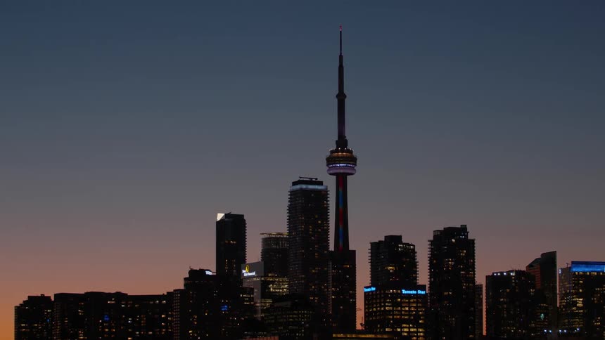 The iconic Toronto skyline featuring the CN Tower is illuminated against the colorful sky at dusk