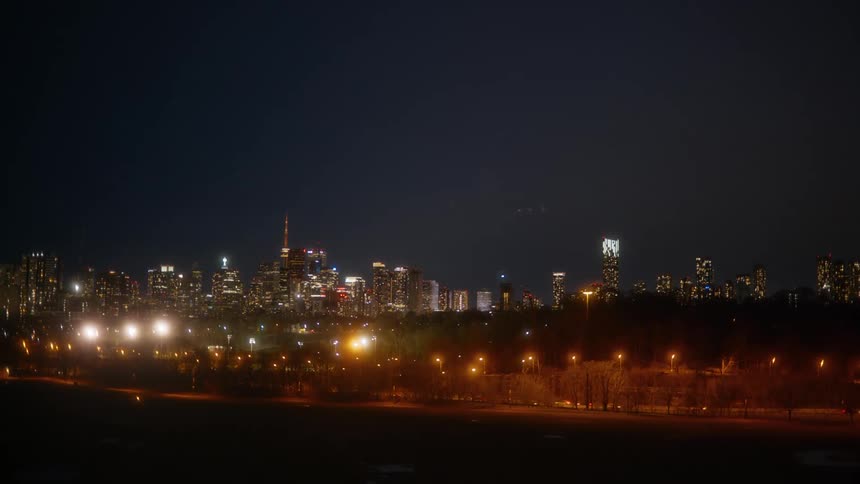 Tilting down from the dark night sky to reveal the brilliantly lit Toronto city skyline and highway traffic