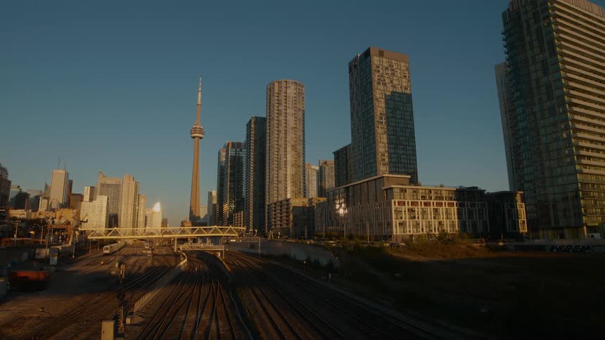 Busy trains travel along railway tracks in front of the iconic Toronto skyline during a golden hour sunset timelapse