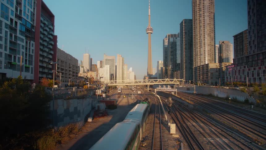 A green and white GO Train travels along the railway tracks towards the Toronto skyline with the CN Tower at sunset
