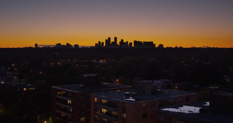 A wide shot with a slow zoom out of a city skyline at sunset, viewed from over the rooftops of residential apartments
