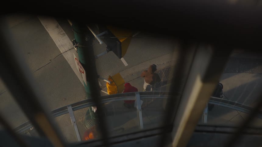 A high-angle view through a window shows pedestrians and traffic at a sunlit city street corner