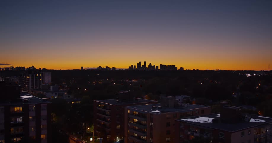 A distant city skyline is silhouetted against a vibrant orange and purple sunset sky as seen from a residential neighborhood