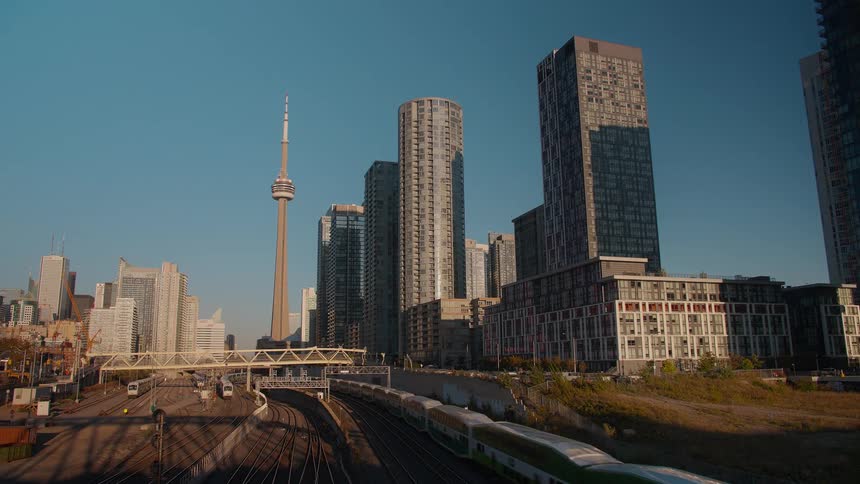 A commuter train travels along the railway with the iconic Toronto skyline and CN tower in the background on a sunny day