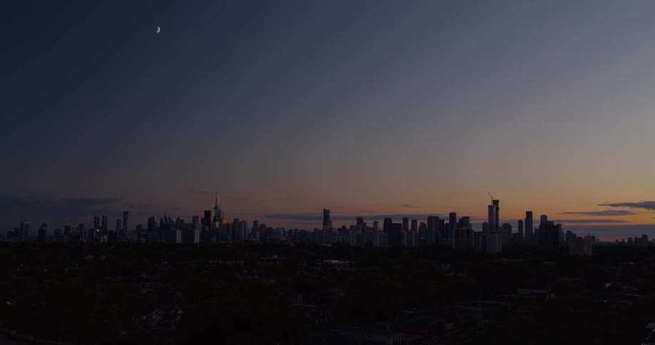 Time-lapse footage captures the transition from a beautiful golden sunset to night over a city skyline, with a crescent moon remaining visible