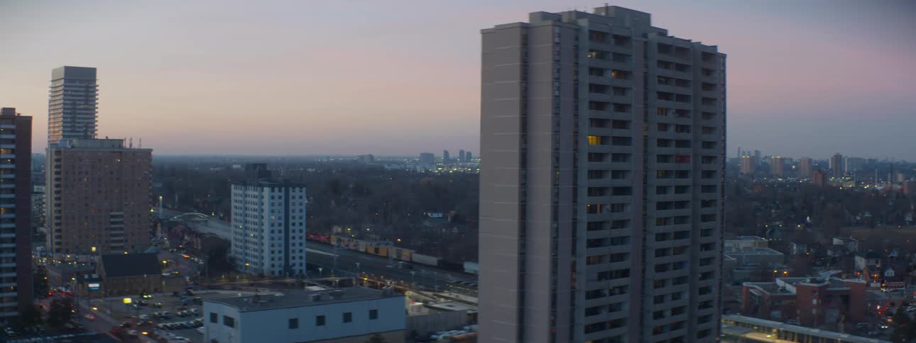 A freight train passes through a city neighborhood with tall apartment buildings during a calm twilight