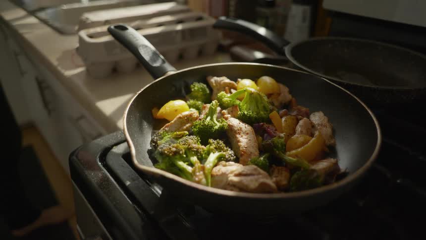 A delicious stir-fry of chicken and vegetables simmers in a pan on a gas stovetop in a sunlit kitchen