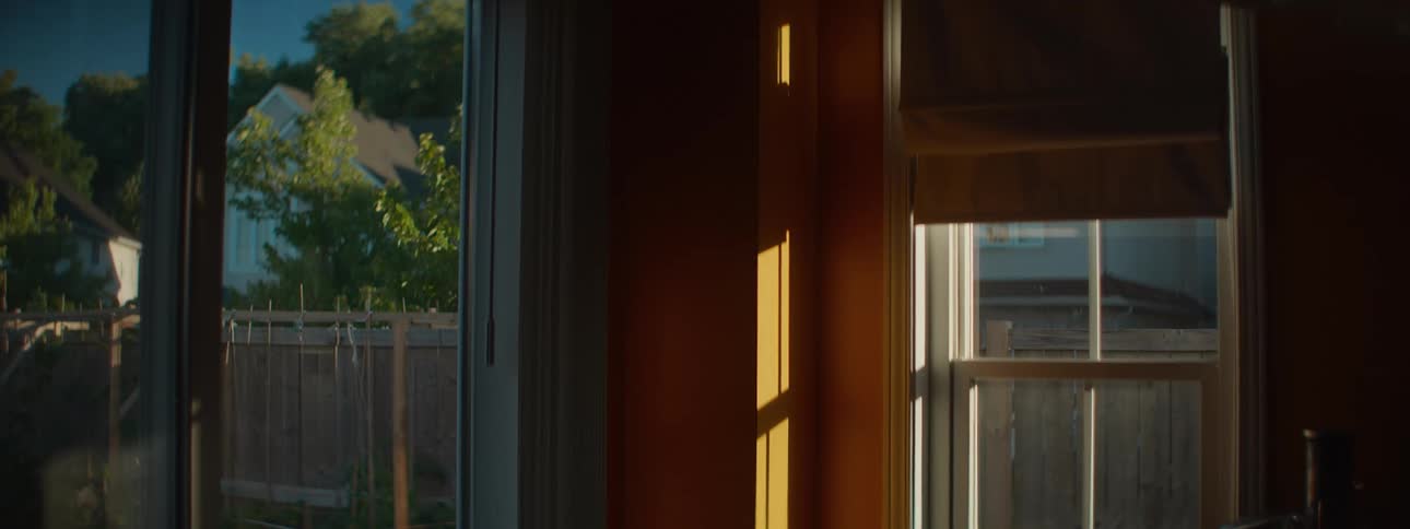 Golden hour sunlight streams through the windows of a quiet suburban home, casting warm light on an interior wall
