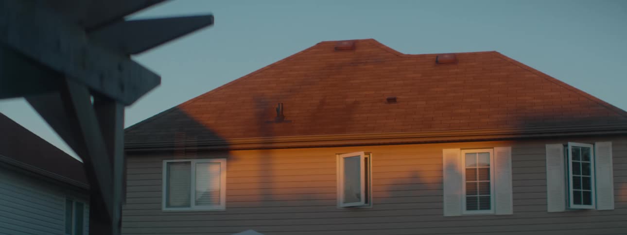 The upper story of a suburban house is bathed in warm golden hour light with one window open