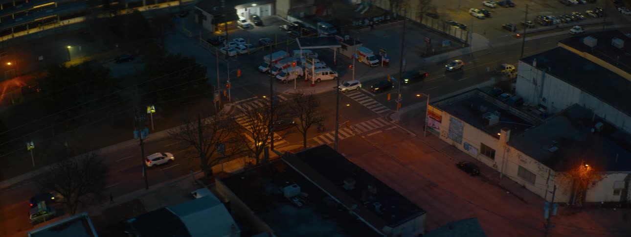 A high-angle, wide shot captures the flow of traffic at an urban intersection next to a gas station at night