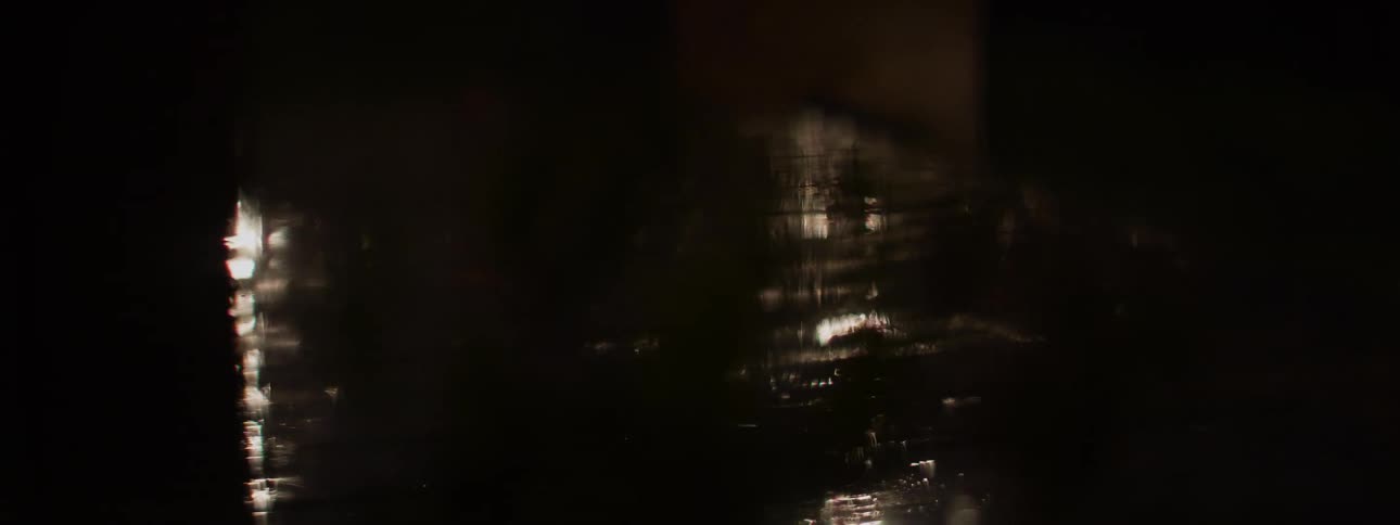 Eerie, abstract reflections of light shimmer across a dark, wet surface at night