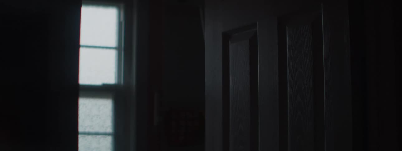 A mysterious shot of a closed wooden door in a dark room with natural light coming from a nearby window