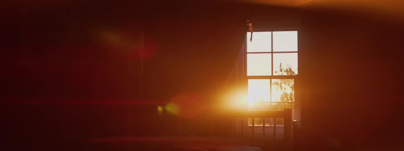Warm, golden hour sunlight streams through a bedroom window, creating a beautiful lens flare