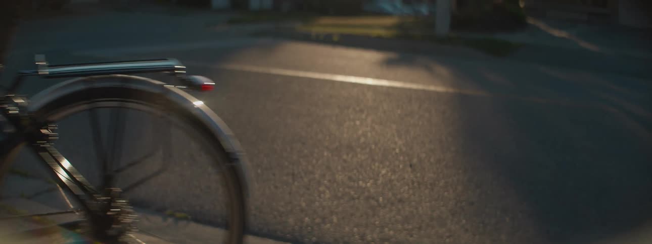 A cyclist rides down a residential street as the camera follows the spinning wheels in the warm evening sunlight