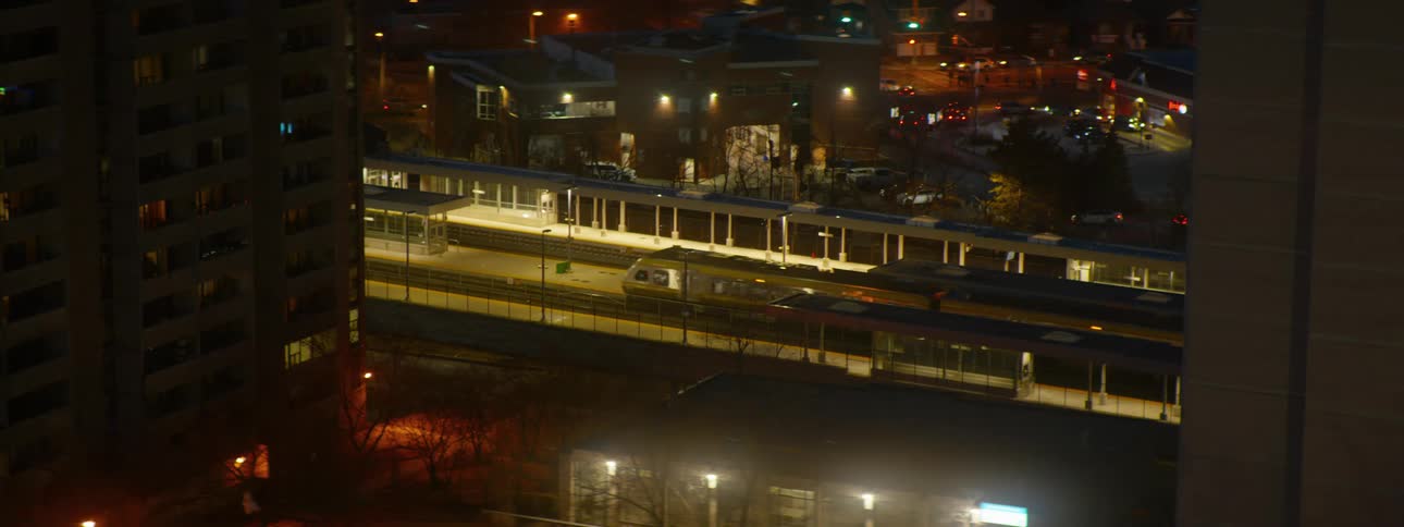 A commuter train leaves the station at night, seen from an aerial perspective