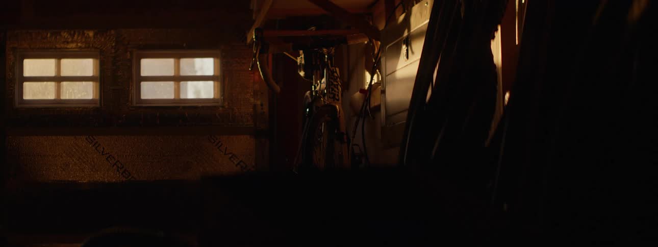 Golden morning light gradually illuminates a bicycle hanging in a dusty, rustic shed
