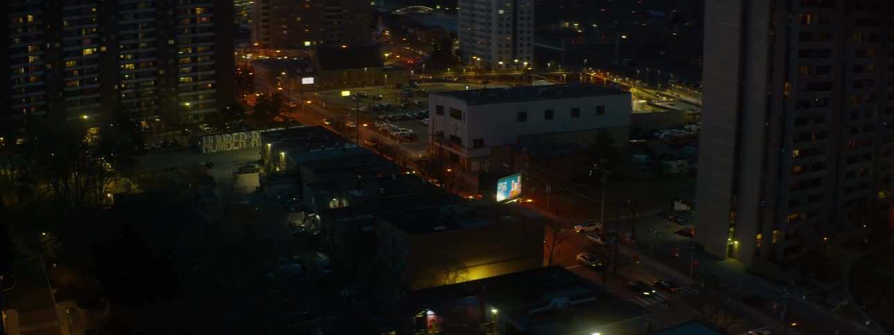 An establishing shot of an urban neighborhood at dusk, zooming out to reveal apartment buildings and traffic below