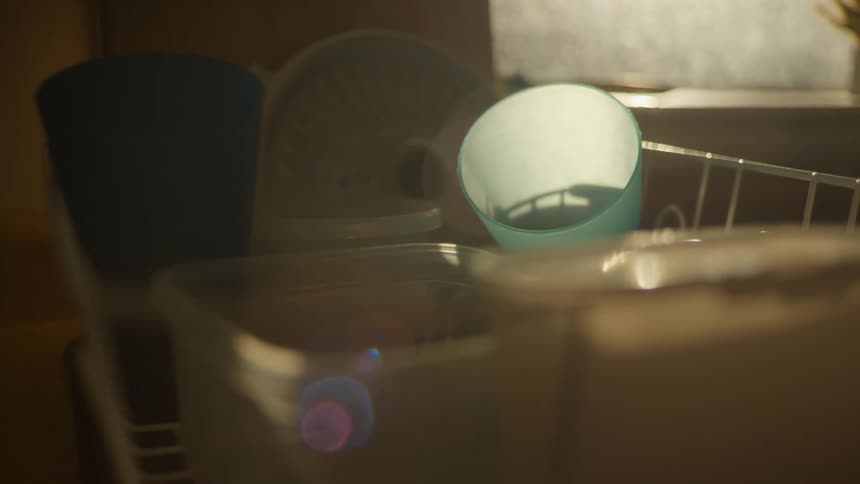Clean plastic kitchenware dries in a dish rack with a soft, hazy light creating a lens flare