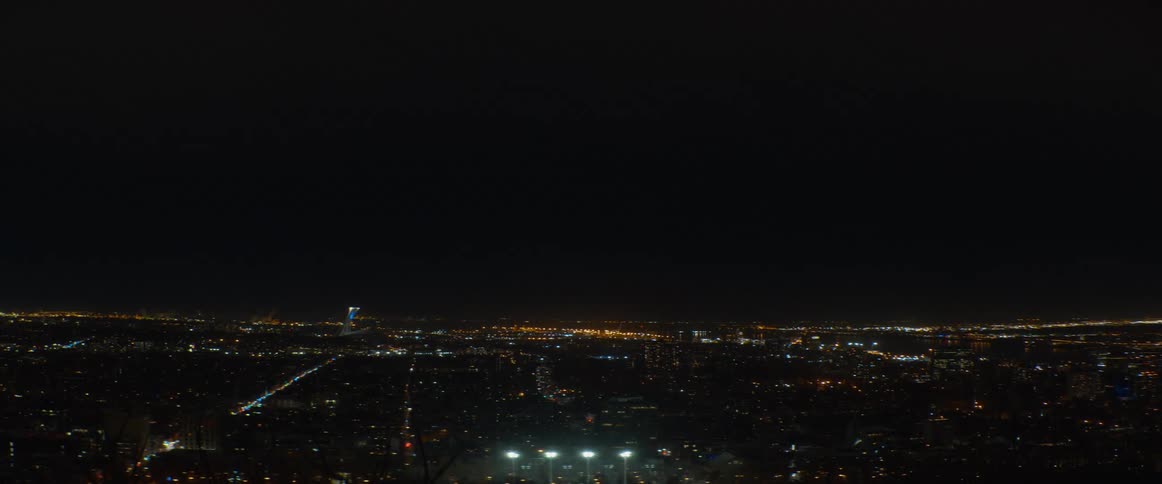 A static high-angle view captures the twinkling lights of a sprawling city against the dark night sky