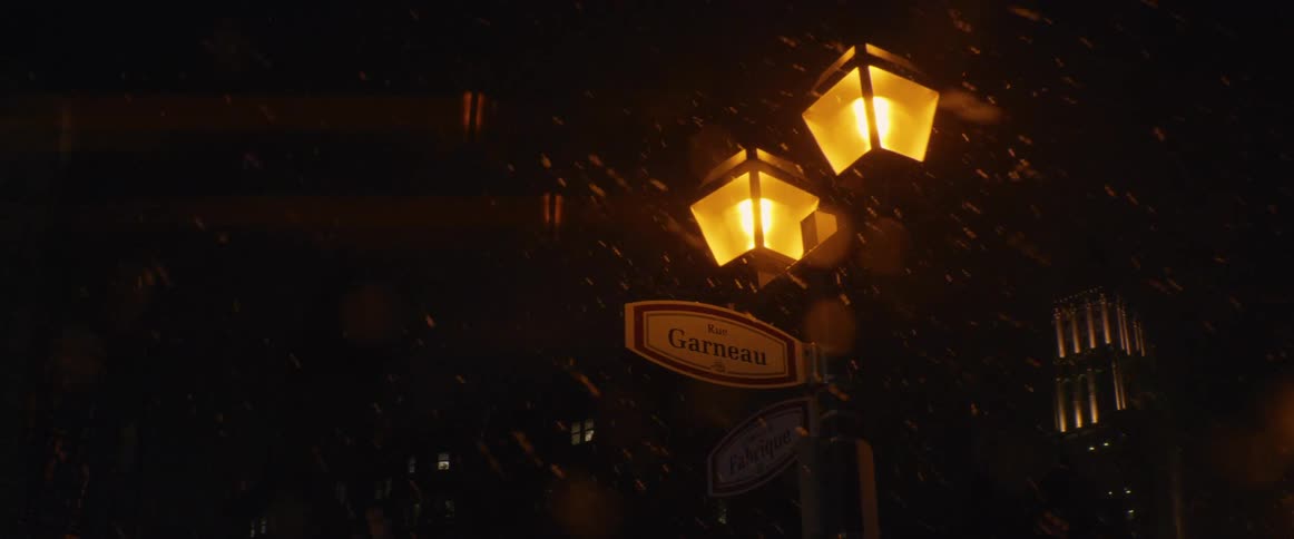 A classic street lamp with French signs glows warmly as snow falls heavily during a dark winter night in the city