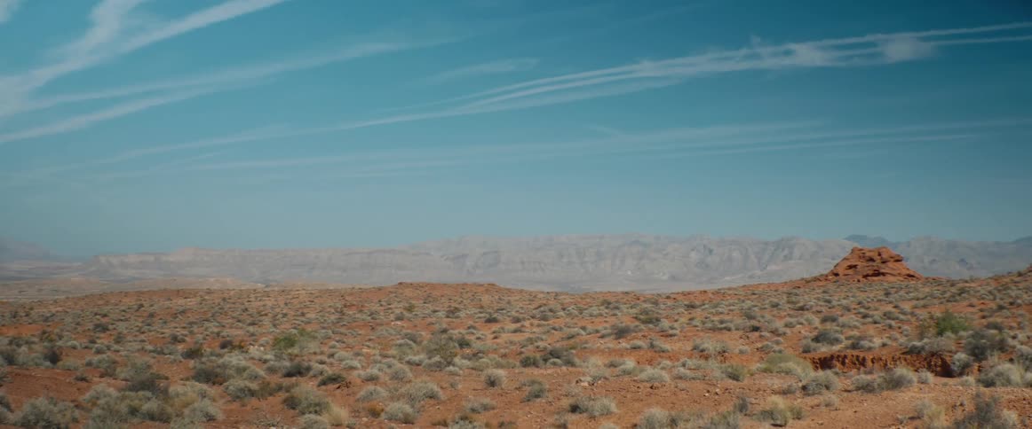 A wide shot of a vast desert landscape under a clear blue sky with distant mountains on the horizon