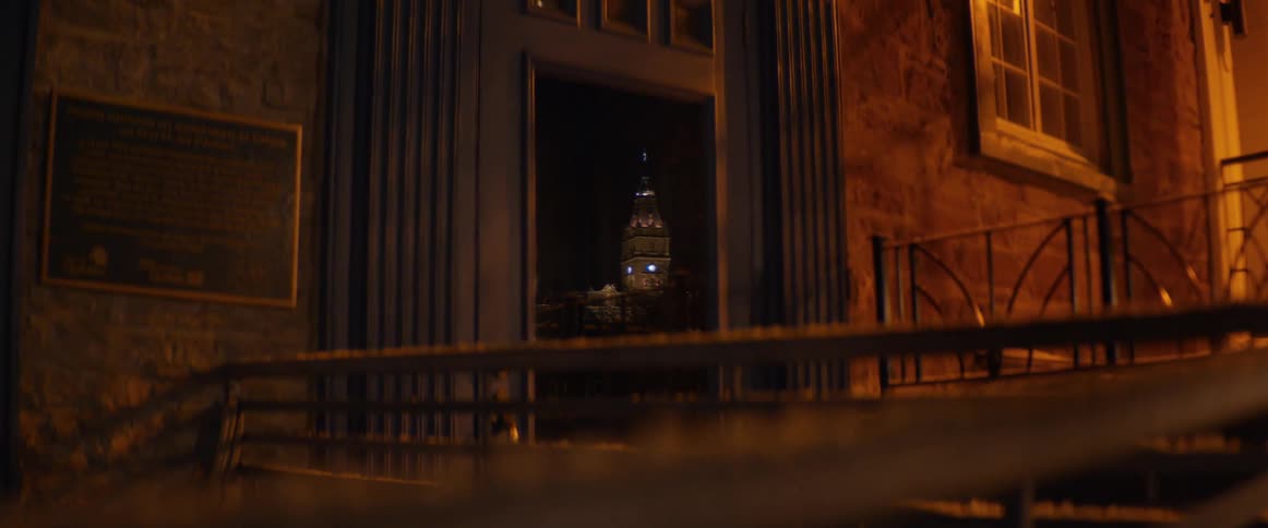 A distant, illuminated clock tower is perfectly framed by the entrance of a stone building at night