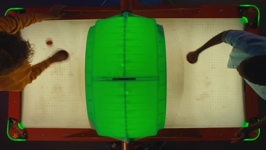 A vibrant top-down view captures two friends engaged in a competitive game of air hockey at an arcade