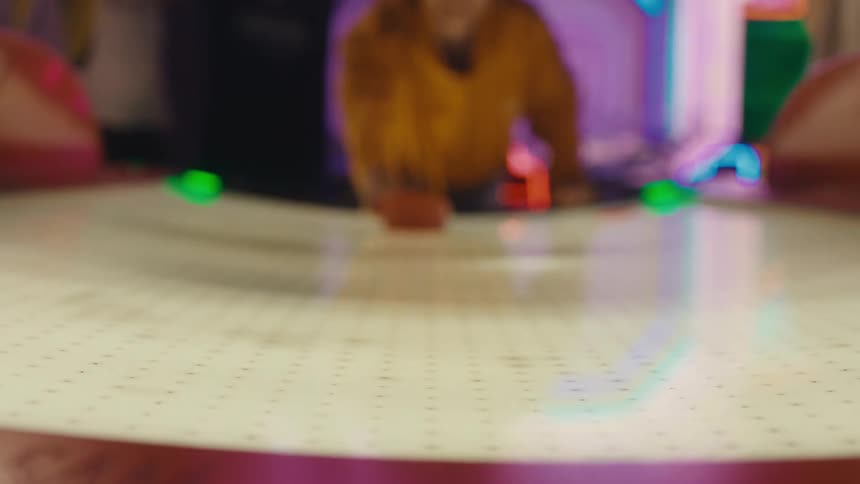 A young man scores a goal while playing air hockey with his friends in a neon-lit arcade, filmed in slow motion from the table's perspective