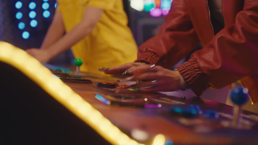 A close-up of a person's hands with long nails energetically playing a classic video game on an arcade machine