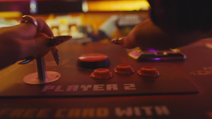 A gamer with stylish nails frantically moves the joystick and mashes the buttons on a Player 2 arcade console